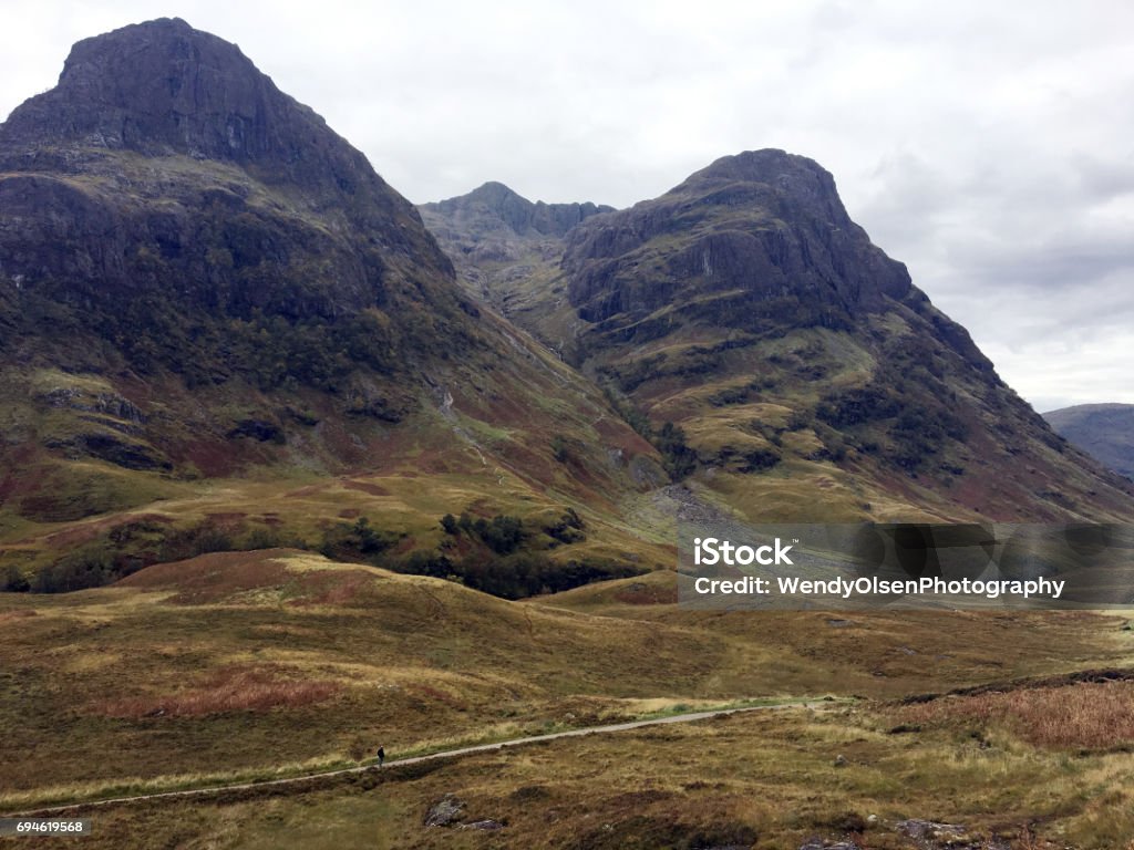 Scenery in Glencoe Scotland Tall rough peaks in the Glencoe area of Scotland. A person can be seen walking along a trail at bottom of picture. Footpath Stock Photo