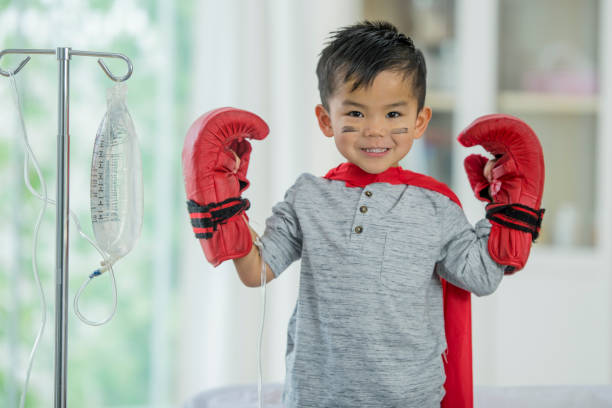 Fighter A young Asian boy is indoors in a hospital. He is wearing casual clothing, a cape and boxing gloves. He looks determined to fight his disease. iv drip photos stock pictures, royalty-free photos & images