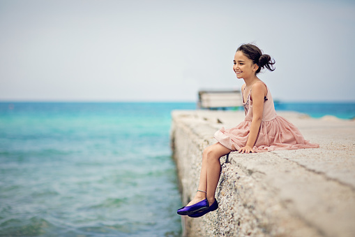 Little girl is sitting on the pier and enjoying the view