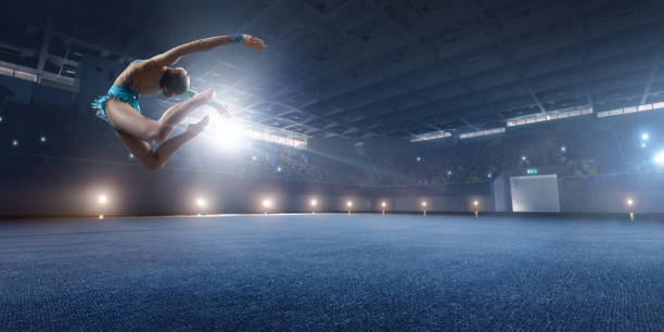 A gymnast girl makes a leap on a large professional stage. She is wearing a professional swimsuit for gymnastics. Behind her is a stadium with spectators.