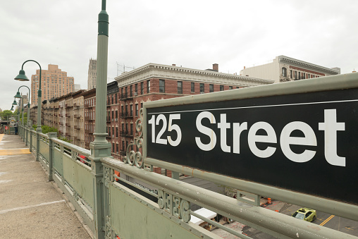 This is a royalty free stock color photograph of the platform of the 125th Street station in the Harlem neighborhood of urban travel destination New York City, USA.  A large sign marks the location. A man stands at the end of the platform. Photographed with a Nikon D800 DSLR in spring.