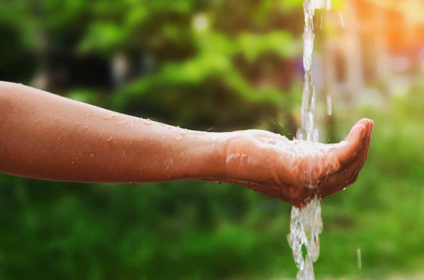 istock Water pouring splash in hand and nature background 694729906