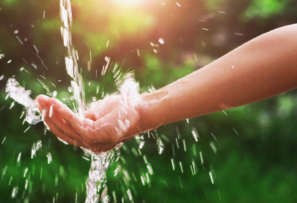 istock Water pouring splash in hand and nature background with sunshine 694729912