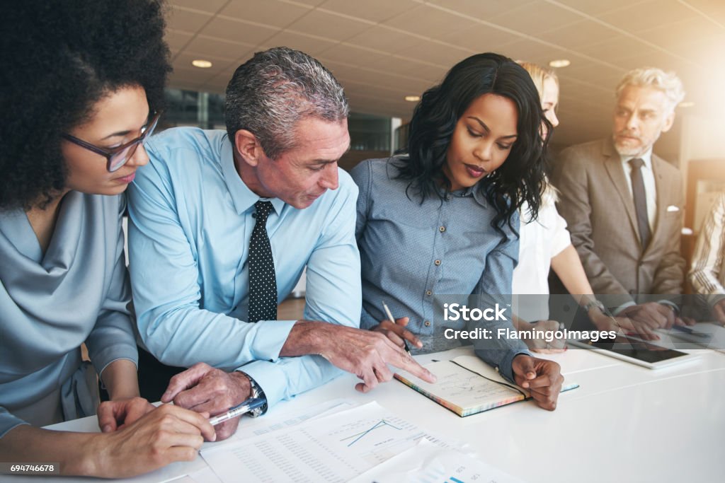 Multiracial workers discussing papers sitting in office Black and white group of people doing teamwork in contemporary office. Multiracial Group Stock Photo
