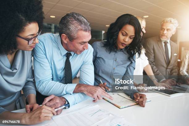Multiracial Workers Discussing Papers Sitting In Office Stock Photo - Download Image Now