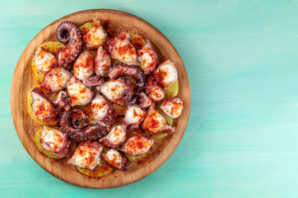 Pulpo a la gallega, traditional Spanish Galician dish An overhead photo of pulpo a la gallega, an octopus with boiled potatoes, typical Spanish dish, on a traditional wooden plate on a teal background with a place for text galicia stock pictures, royalty-free photos & images