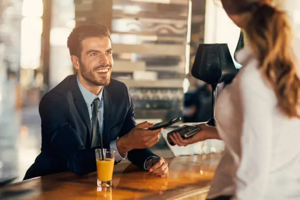 Businessman paying via smart phone at a bar counter.