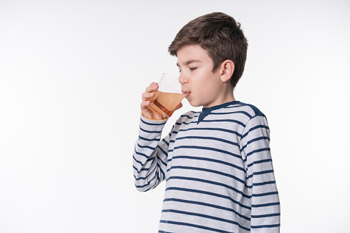 The ill little boy is drinking water with pill over white background.