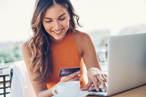 Beautiful young woman with credit card and laptop in cafe