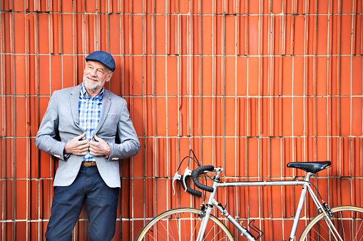 Handsome senior man in blue checked shirt and gray jacket with bicycle. Orange brick wall background.