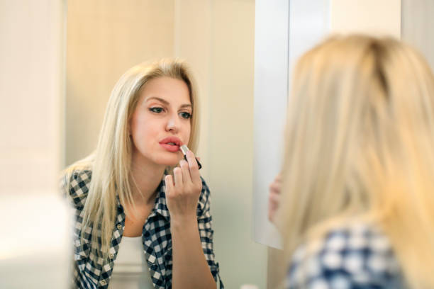 istock Blonde woman putting on lipstick 694828262