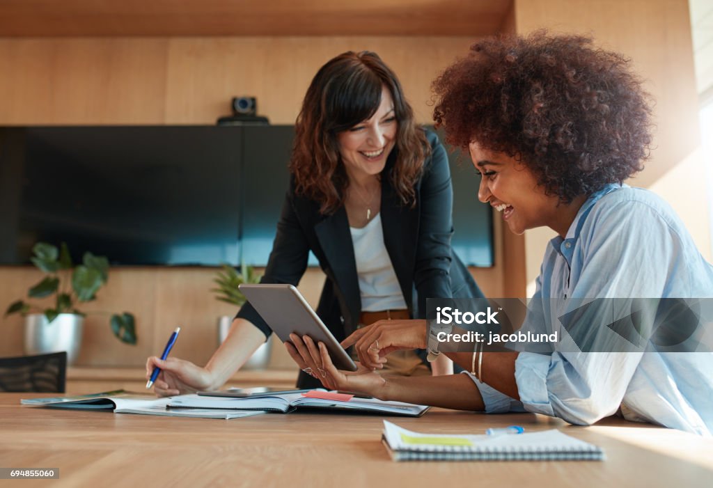 Creative female executives using digital tablet in office Shot of two young woman working together on digital tablet. Creative female executives meeting in a office using tablet pc and smiling. Working Stock Photo