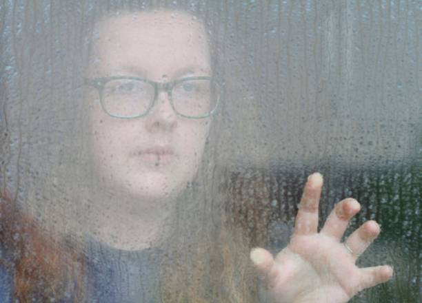istock Young woman looking through window on rainy day 694897410