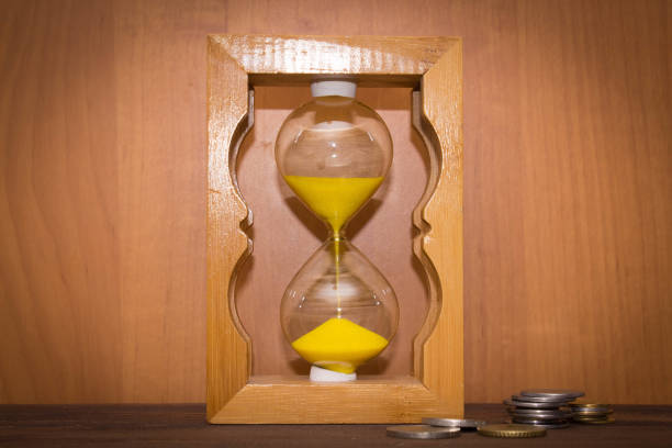 istock The glossy old-style hourglass standing with a coins 694903448