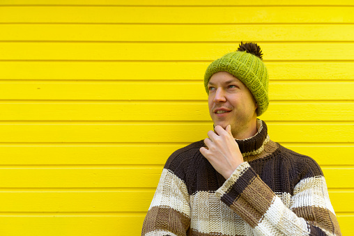 Young happy handsome man smiling while thinking against yellow-painted wooden wall horizontal shot