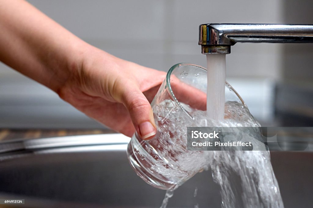 Drinking Water Female hands pouring water in glass cup from a kitchen faucet. Woman hand's filling the glass of water. Filling glass of water from stainless steel kitchen faucet Faucet Stock Photo