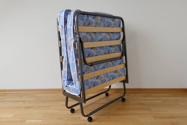 A folding bed in front of a white wall an a blue mattress\