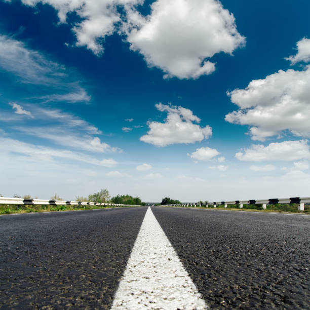 istock asphalt road closeup with white line on center and low dramatic clouds in blue sky 694924122
