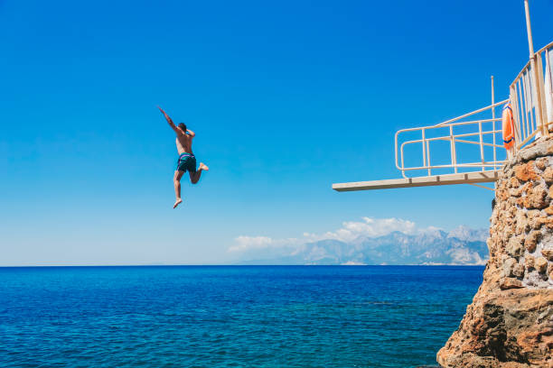 joven, salto de trampolín en las rocas al mar - salto desde acantilado fotografías e imágenes de stock