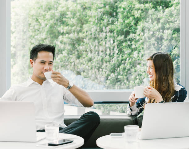 istock Young Asian couple or coworkers having coffee break while working on laptop computer at cafe or coffee shop. Leisure, casual work, love, or friendship concept. With copy space 694950568