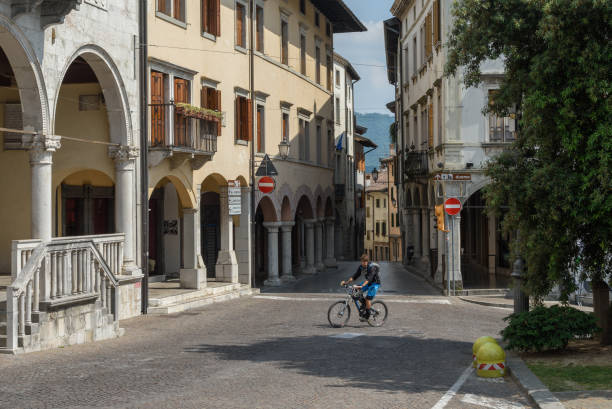 Gemona del Friuli,City Hall Main Street Gemona,Friuli, Italy - June 02, 2017: A cyclist runs through the main street of Gemona in front of the town hall gemona del friuli stock pictures, royalty-free photos & images