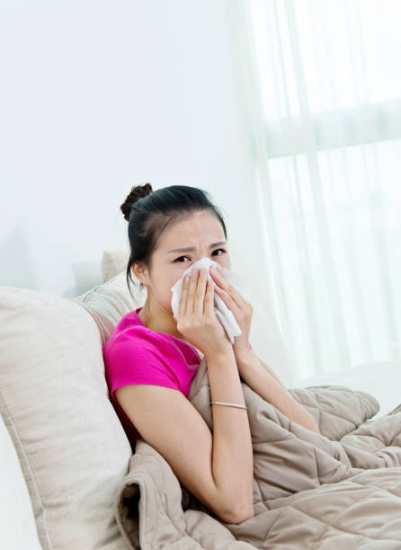 istock Sick woman blowing her nose on sofa 694982620