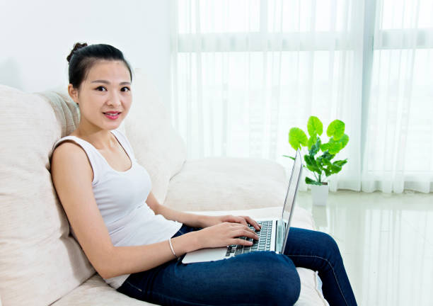 istock Young asian woman sitting on sofa with laptop 694982970