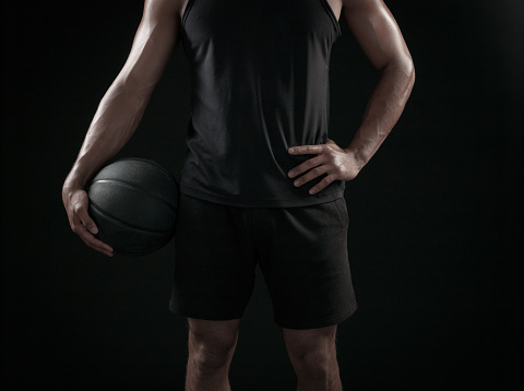 Man Holding a Basketball On A Black Background in dramatic lighting.