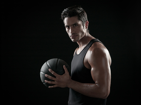 Man Holding a Basketball On A Black Background in dramatic lighting.