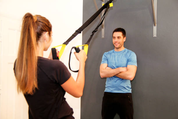 Beautiful pretty fitness sporty woman with help of her personal trainer exercising with a resistance band in a gym club. Sportswoman training with trx resistance band with trainer in sports center. mujer deportivo de fitness bastante hermosa con ayuda de su entrenador personal, hacer ejercicio con una banda de resistencia en un club de la gimnasia. entrenamiento con banda de resistencia trx con entrenador en polideportivo de deportista.
