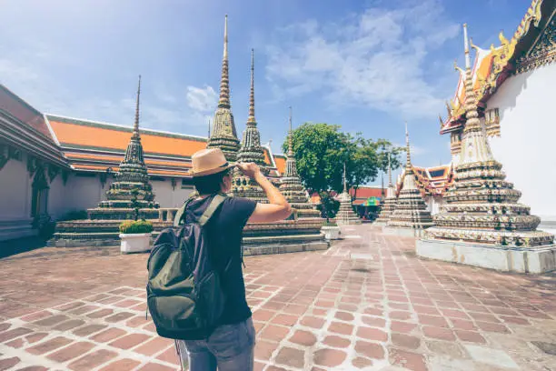 Photo of Young man traveler with backpack and hat looking the map with Grand palace and Wat phra keaw at Bangkok Thailand