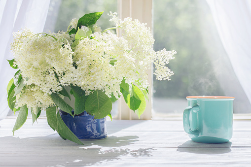 Elder flowers and cup of hot coffee by the sunlight window in the morning