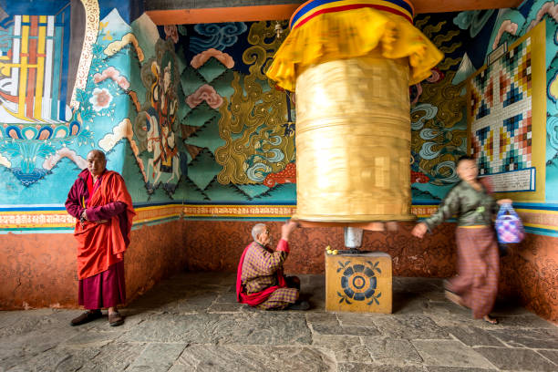 an old bhutanese female at the temple praying at prayer wheel