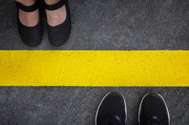 Legs of a couple standing opposite each other Legs of a couple standing opposite each other divided by the yellow asphalt line top view boundary stock pictures, royalty-free photos & images