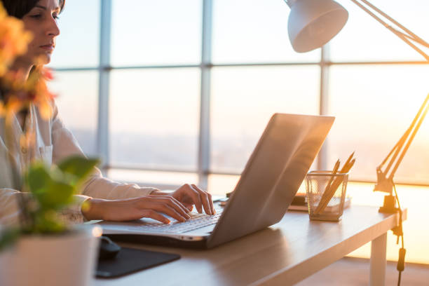 istock Side view photo of a female programmer using laptop, working, typing, surfing the internet at workplace. 695137156