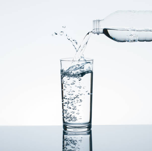 istock Pouring drinking water from bottle into drinking glass with water splash on white background 695137576