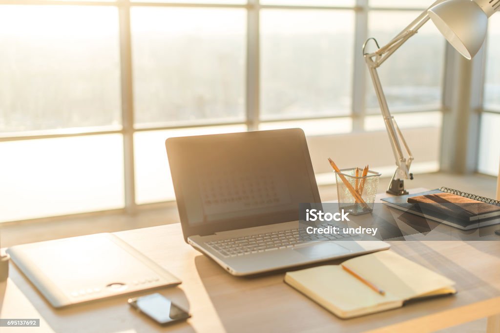 Side view picture of studio workplace with blank notebook, laptop. Comfortable work table, home office. Side view picture of studio workplace with blank notebook, laptop. Designer comfortable work table, home office Desk Stock Photo