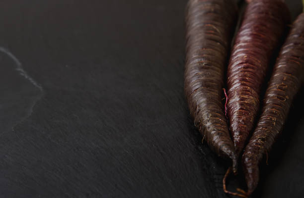 Ripe black carrots. Dark stone background. Autumn harvest. Top view
