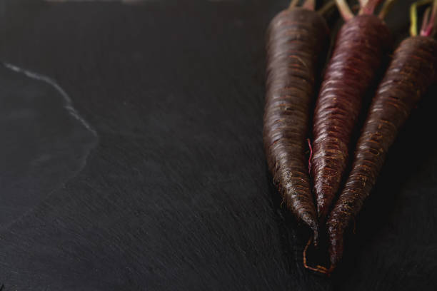 Ripe black carrots. Dark stone background. Autumn harvest. Top view