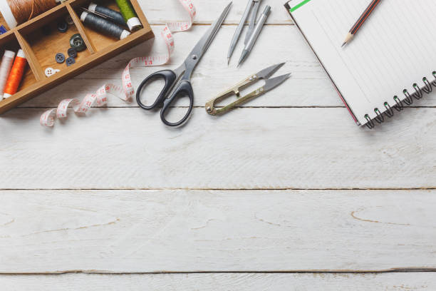 istock Top view accessories tailor concept.Tailor tools is cutting scissors, spools of thread,tape measurement,buttons and sewing clothes. Notebook for free space text on rustic wooden background. 695157826