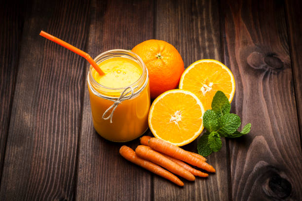 High angle view of a glass jar with orange and carrot juice shot on rustic wooden table. Orange fruits and carrots are beside the jar. Predominant colors are orange and brown. DSRL studio photo taken with Canon EOS 5D Mk II and Canon EF 100mm f/2.8L Macro IS USM