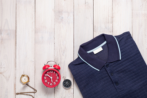 Polo shirt with alarm clock,pocket watch,compass on white wooden background