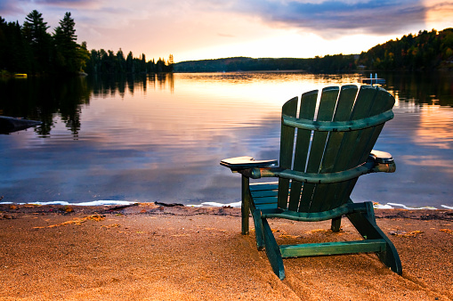 Wooden chair on beach of relaxing lake at sunset