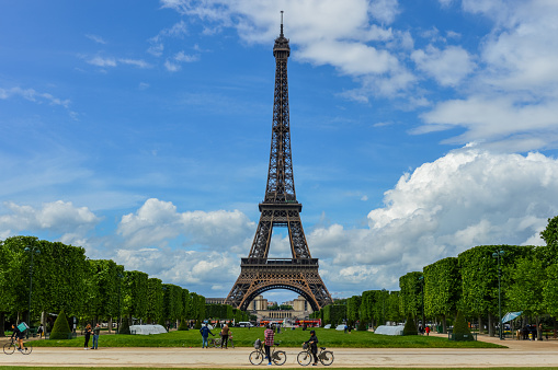 The Eiffel Tower as seen from the Champ de Mars. Photo taken during a warm sping day and there are many people visiting the Tower and enjoying the sunny day on the lawn.