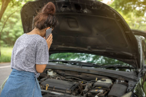 istock Asian woman using mobile phone while looking at broken down car on street 695207552