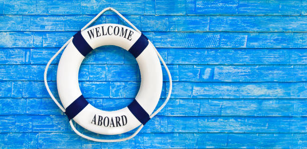 White color Life buoyancy with welcome aboard on it hanging on blue wall. White color Life buoyancy with welcome aboard on it hanging on blue wall. had space on right side for your text. aboard stock pictures, royalty-free photos & images