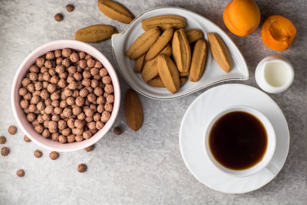 istock Breakfast table with coffee, ginger cookies, chocolate cereal balls, milk, and apricots on stone background. 695224362