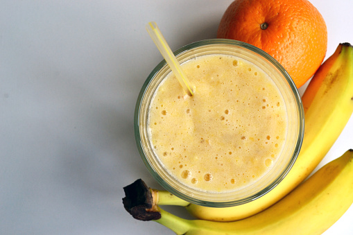 A composition of bananas and orange and a glass with smoothies