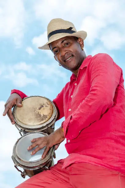 Professional Cuban conga drum player against blue sky, low angle view