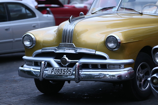 Havana, Cuba- 1/28/2017: Vintage cars are driving on the street. Incidental people on the background.